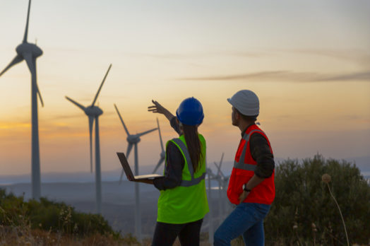 Young maintenance engineer team working in wind turbine farm at sunset